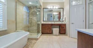 Bathroom with clear shower walls, white bathtub, beige floor tiles, and wood cabinets